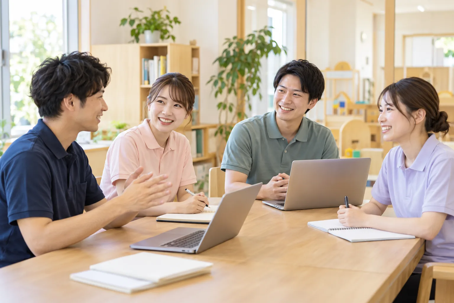 明るいオフィスで、ノートとパソコンを囲んで話し合うスタッフたち